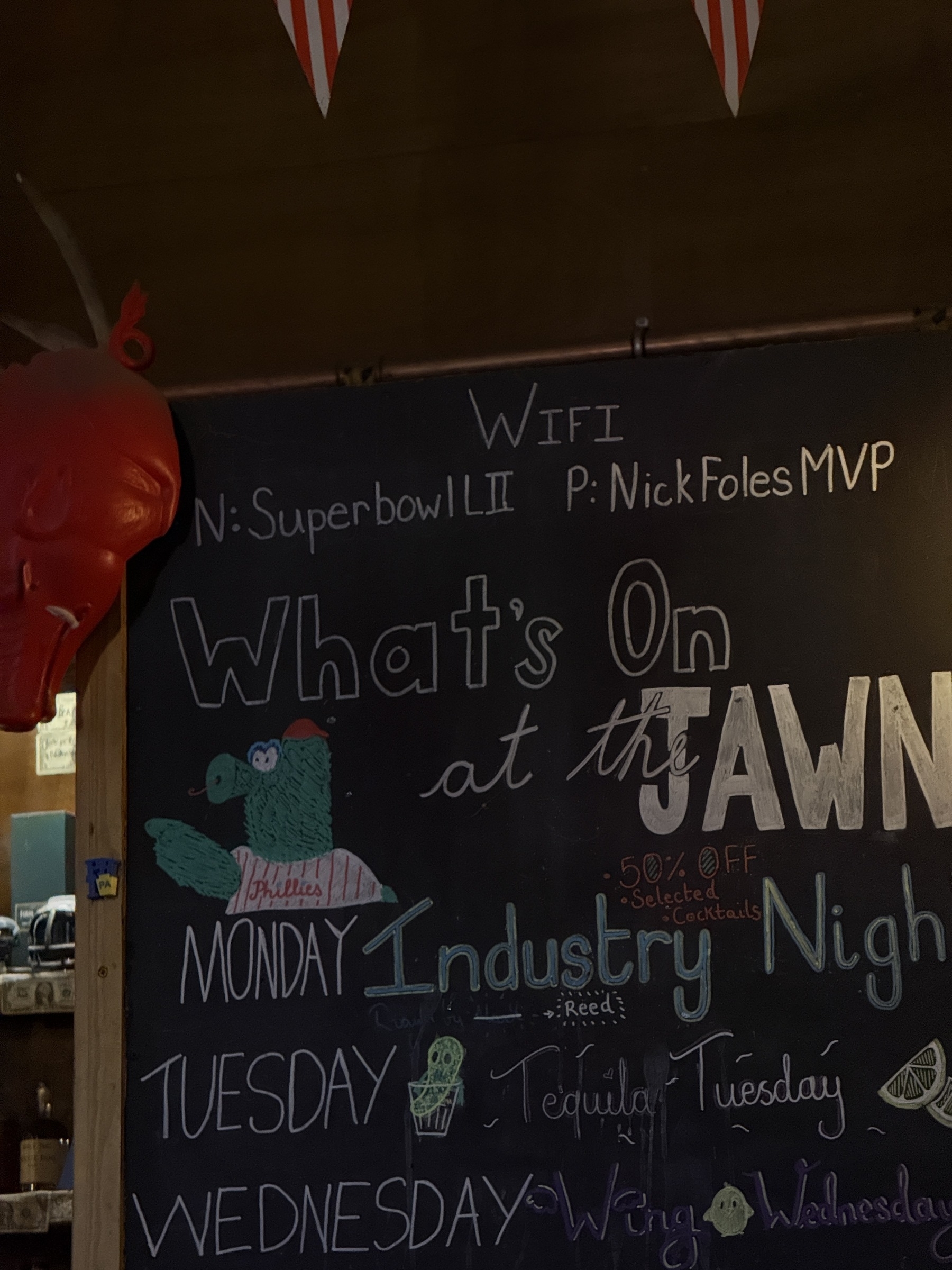 A chalkboard displays a Wi-Fi password, a Super Bowl reference, and weekly specials for a bar called "Jawn," with creative typography and illustrations.